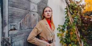 Woman in a tan suede jacket leaning against a weathered vintage door in autumn light