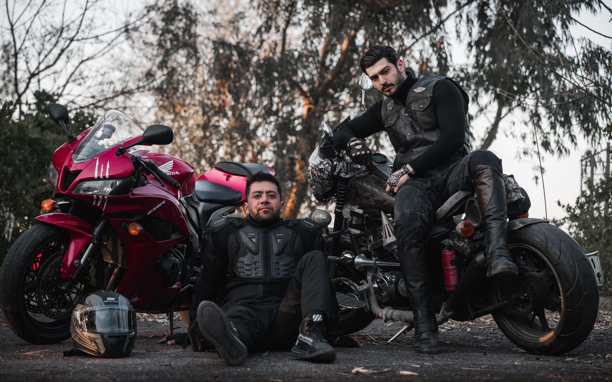 Riders in leather gear standing with a classic motorcycle