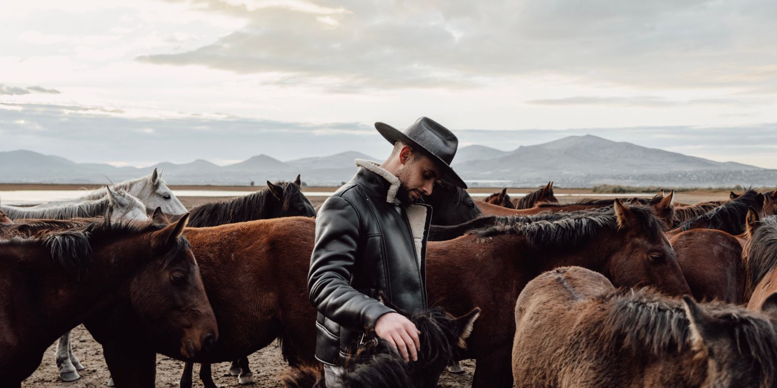 A figure in rugged western leather against an open landscape