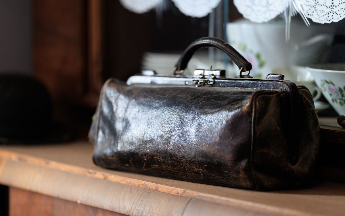 A vintage leather bag resting on a wooden shelf, rich with age