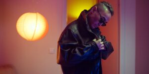 Fashionable man in a black leather jacket adjusts his collar in a stylish indoor setting with ambient lighting