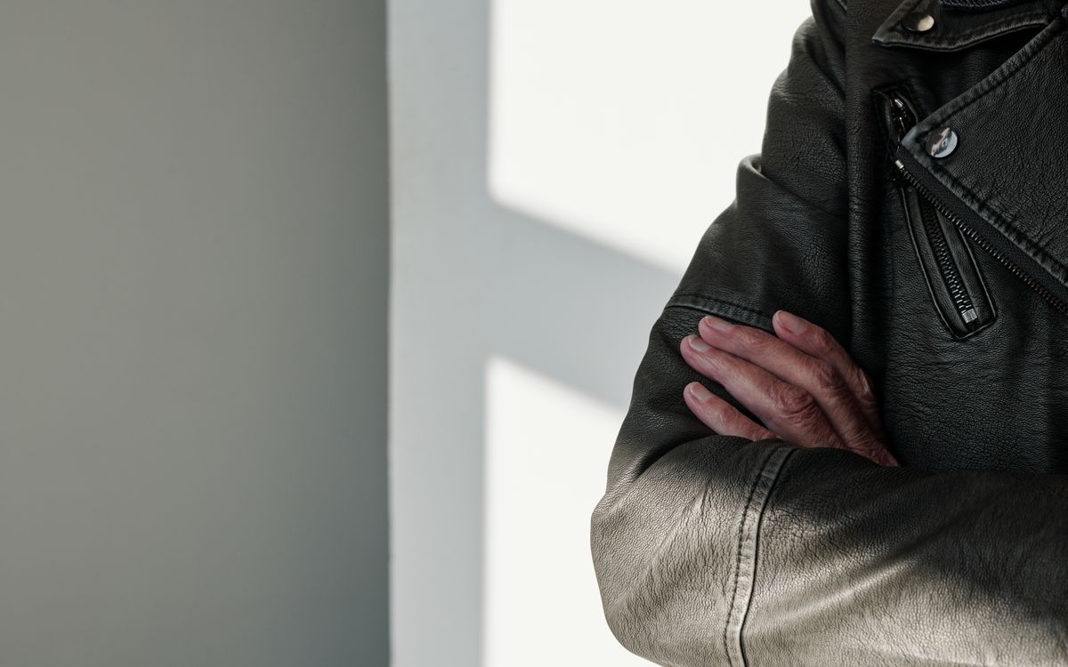 Close up of crossed arms in a black leather jacket with sunlight and shadow