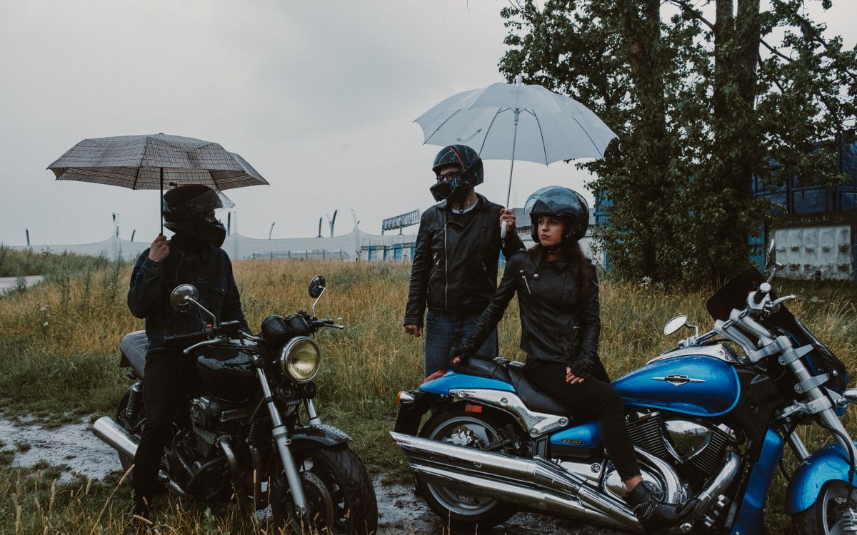 Motorcyclists sheltering from rain under umbrellas in a grassy field
