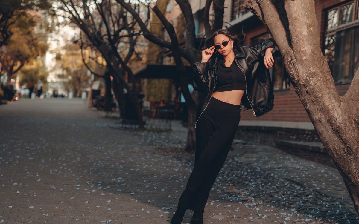 Stylish woman in a black outfit posing in an urban autumn scene with scattered leaves
