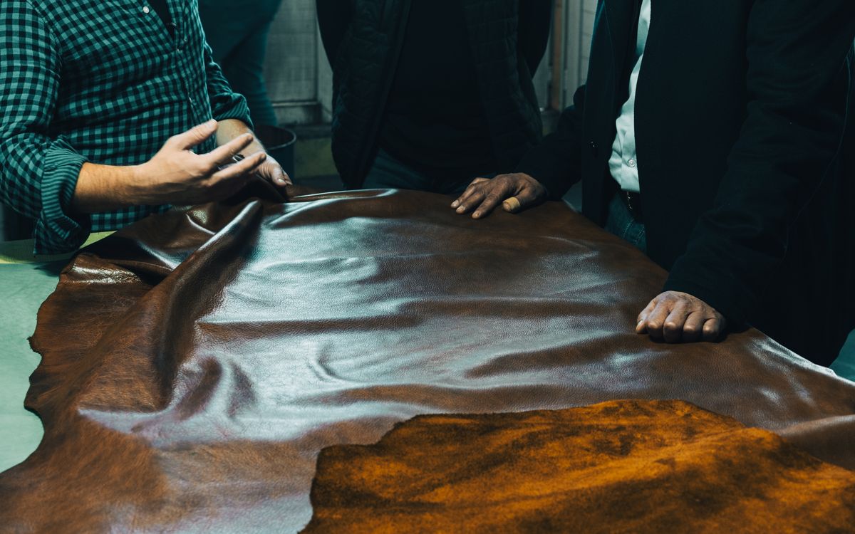 A group of craftsmen examining leather on a table, focused on quality and material selection