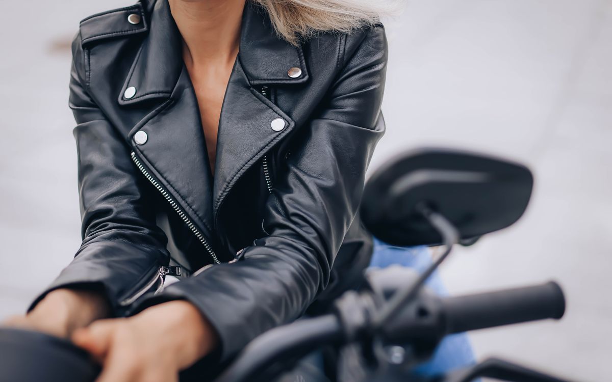 Close-up of a woman wearing a black leather jacket with a stand collar while riding a motorcycle