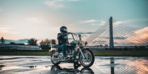 Motorcycle rider in leather gear on a wet road with a bridge in the background during sunset