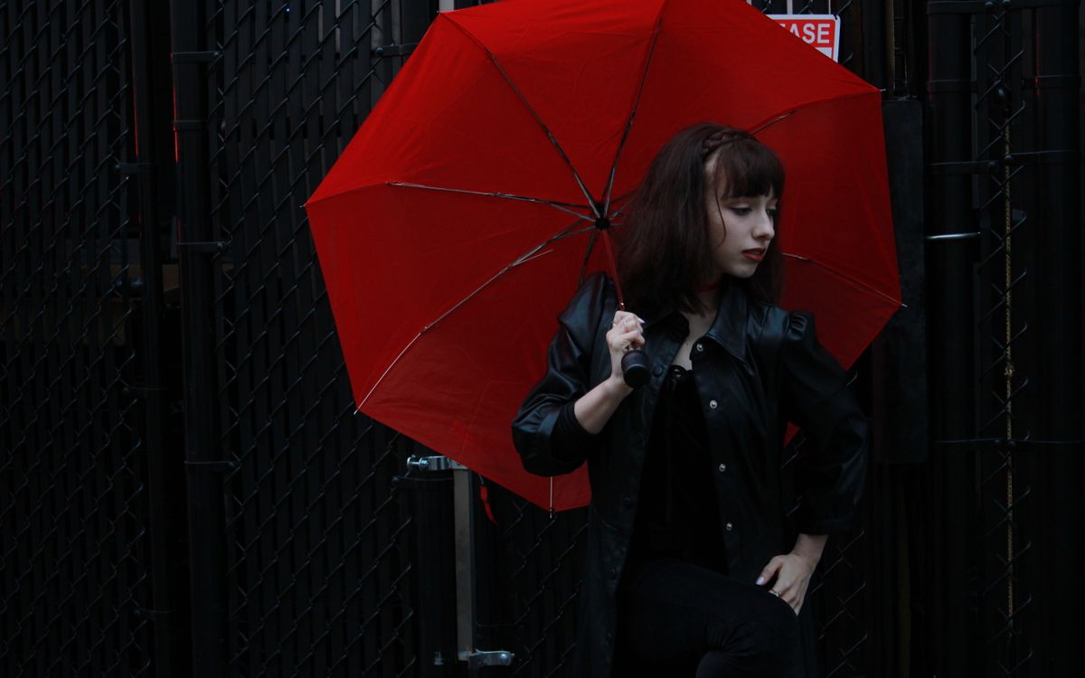 Caucasian woman in black leather jacket with red umbrella outdoors