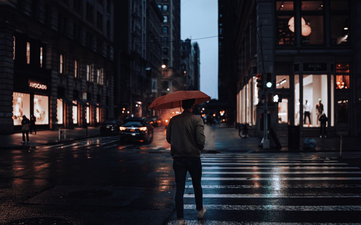 Man walking with red umbrella on rainy city street at night