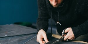 Serious male tailor with scissors cutting circle out of leather material while standing at workbench in atelier