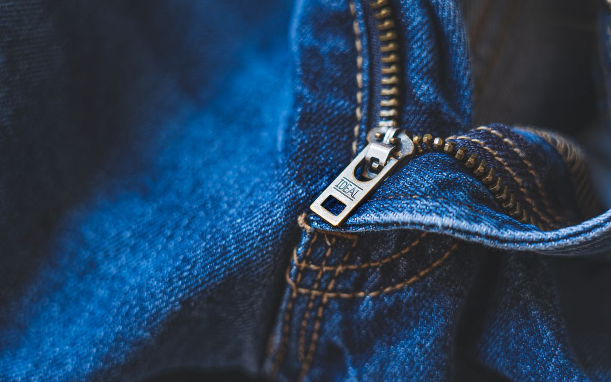 Close-up of blue denim fabric featuring a metal zipper with detailed stitching