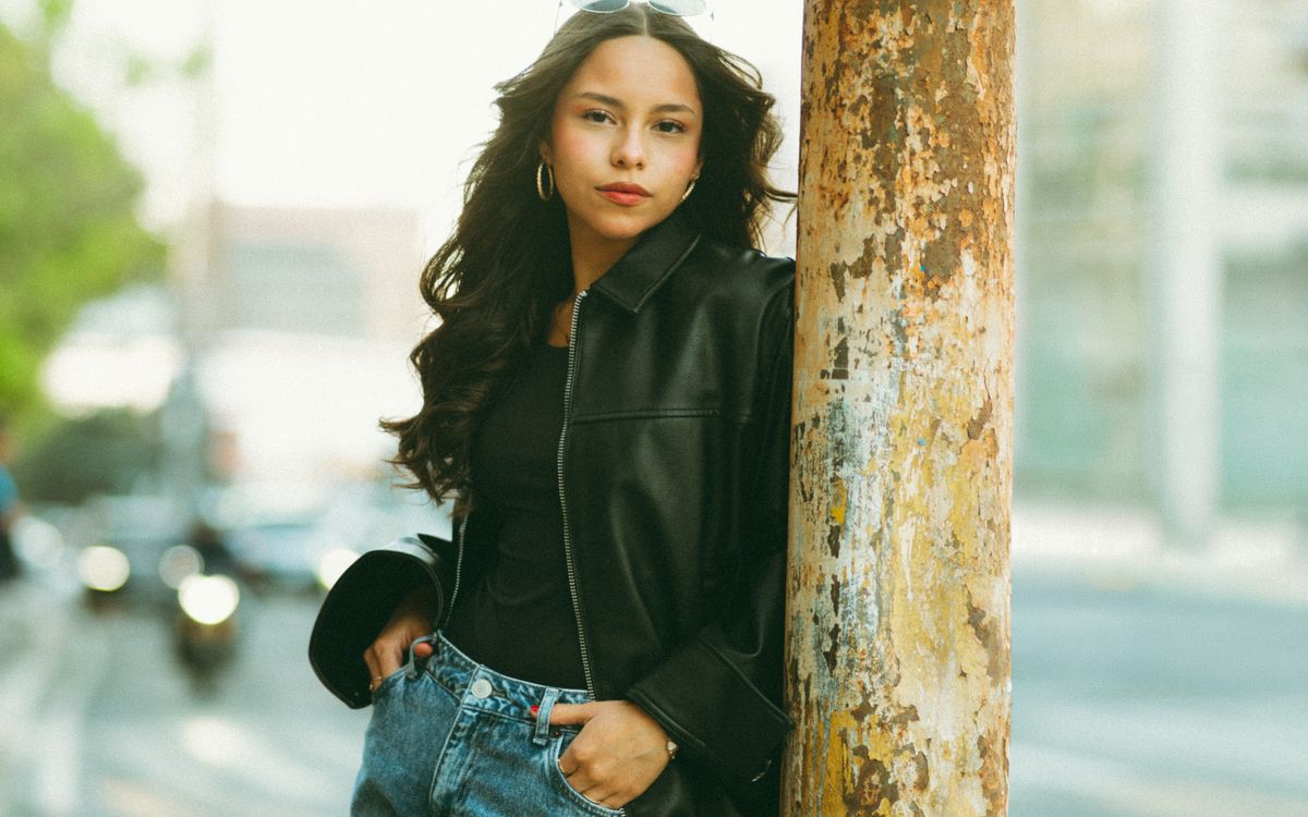 Stylish young woman in leather jacket poses on city street