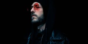 Moody portrait of a man in a black leather jacket and red tinted glasses with a dark background