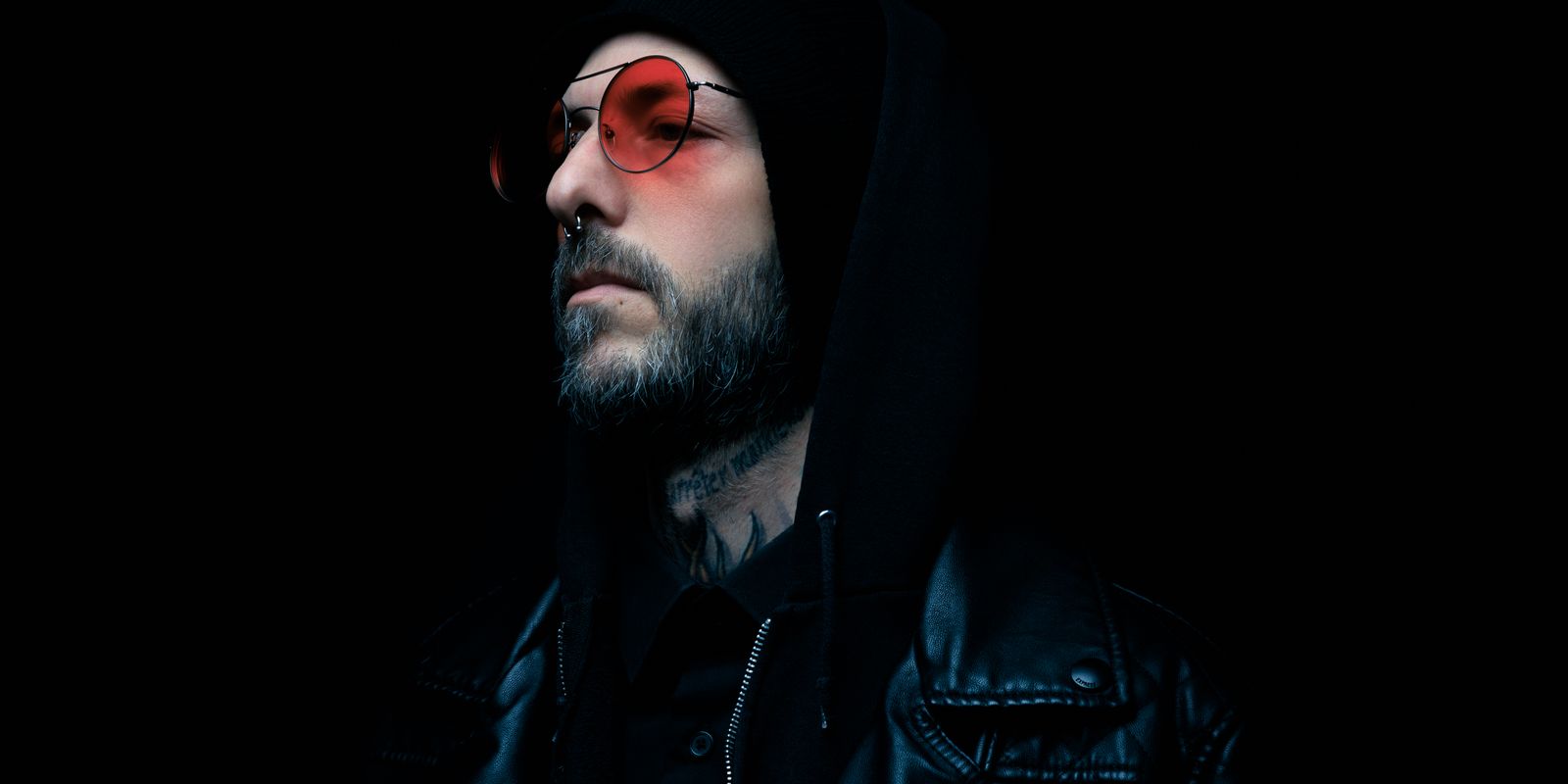 Moody portrait of a man in a black leather jacket and red tinted glasses with a dark background