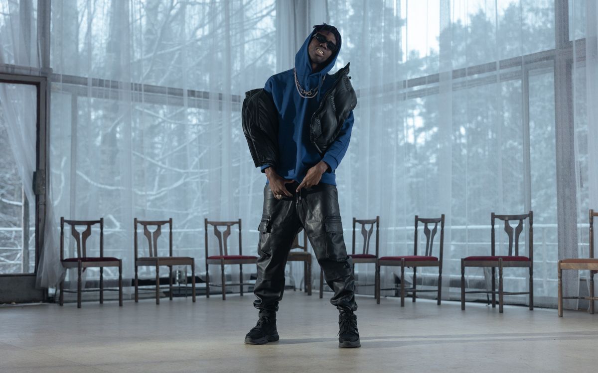 Fashionable man in blue hoodie and leather pants posing indoors with dramatic lighting