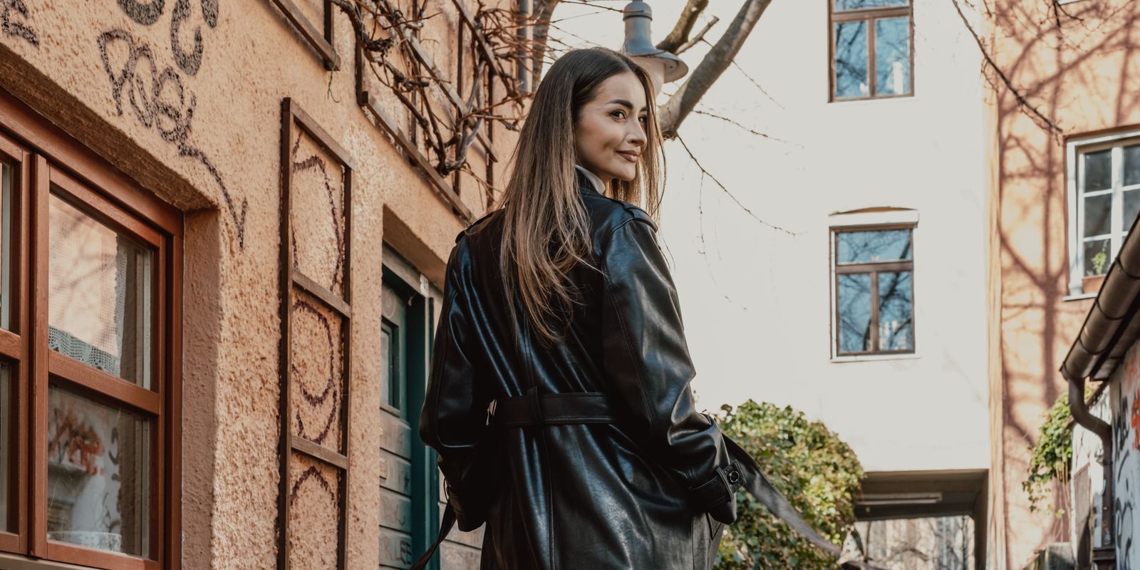 Fashionable woman in a long black leather coat walking a graffiti lined city street