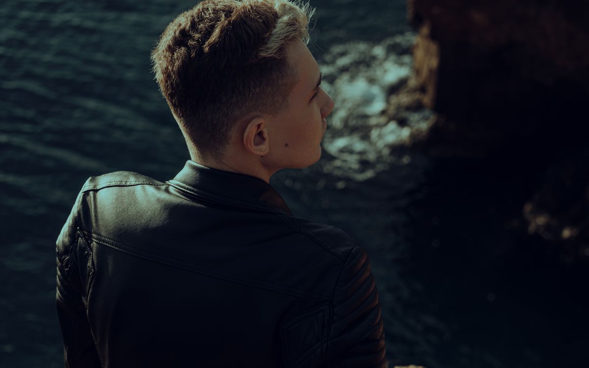 Young man wearing a leather jacket looking out over the sea