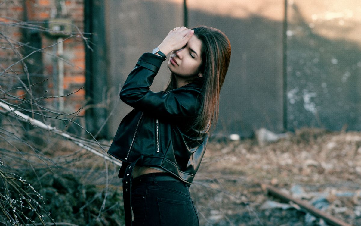 Young woman wearing a leather jacket outdoors with her eyes closed