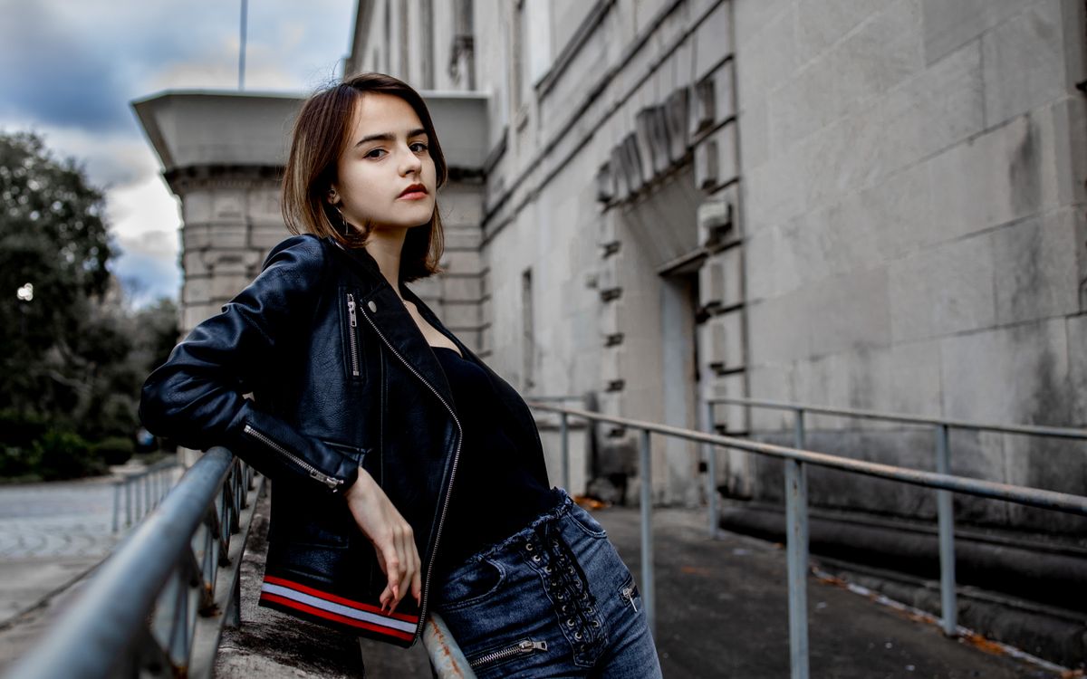 Fashionable young woman posing confidently in a leather jacket against an urban backdrop