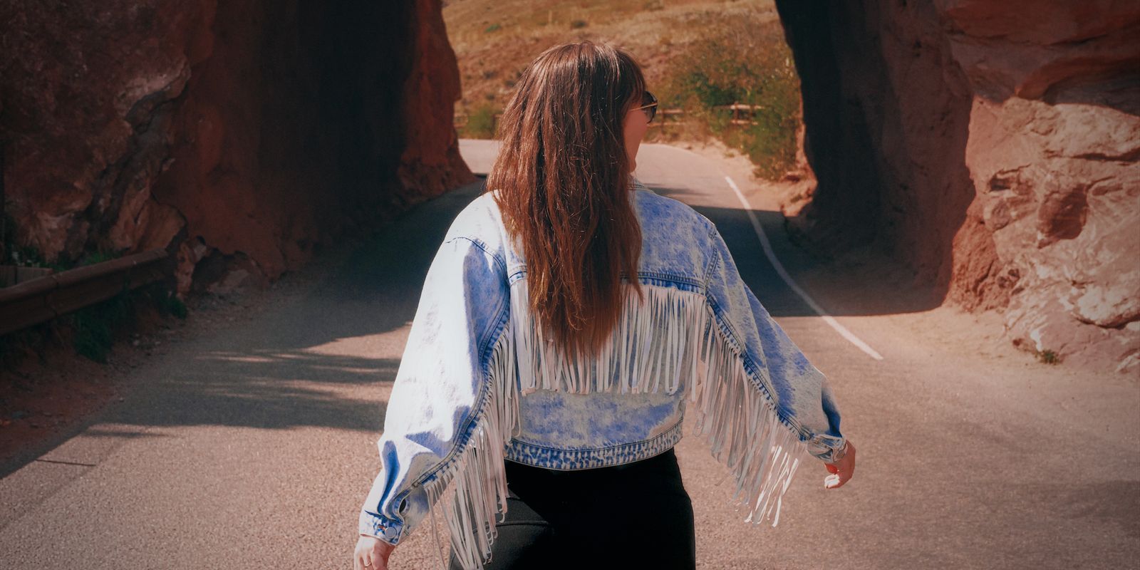 Woman in a fringed jacket walking through a picturesque stone tunnel on a sunny autumn day