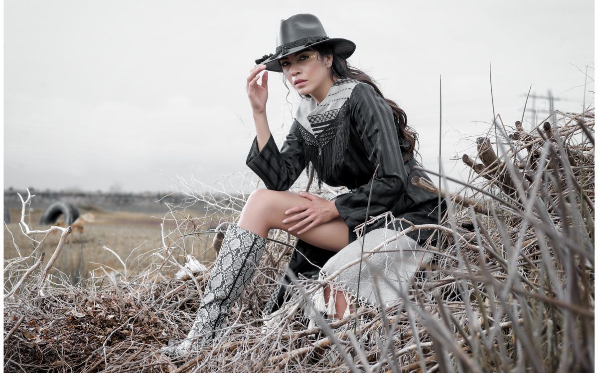 Stylish woman in western attire posing outdoors in a rural field with dry grass