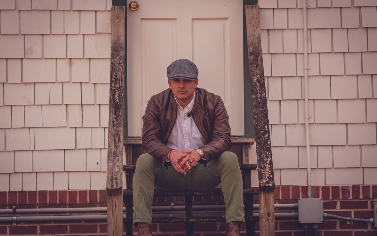 Man in a brown leather jacket sitting on wooden steps outside