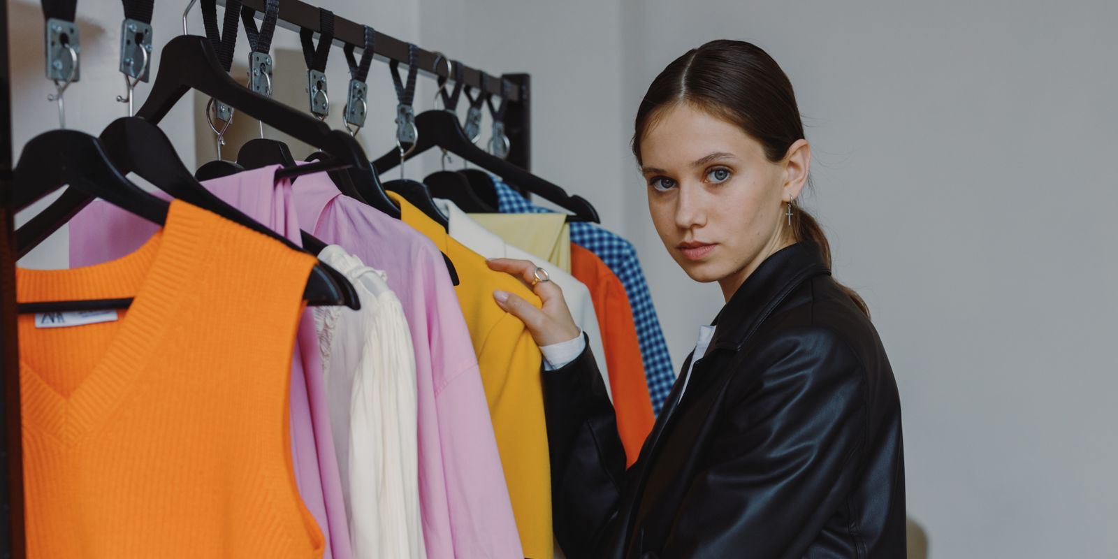 Stylish woman in a black leather jacket browsing clothes on a rack in a bright indoor boutique