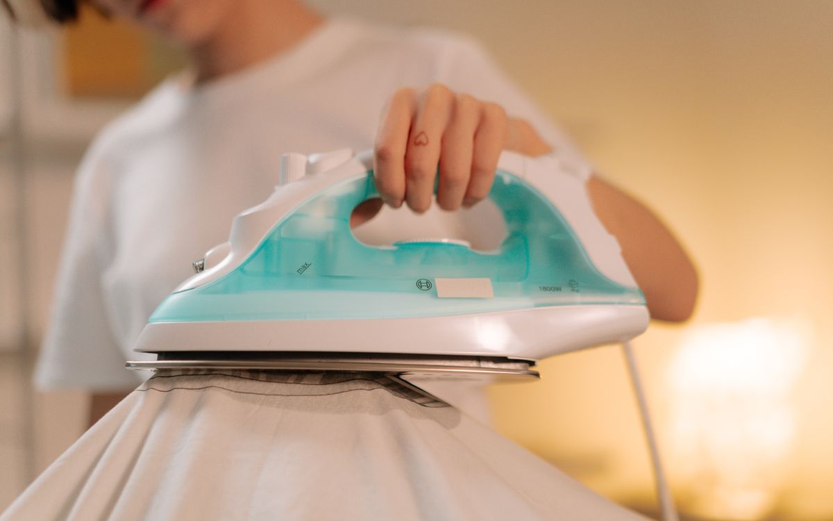 Close-up of a person using a steam iron to smooth a light garment indoors