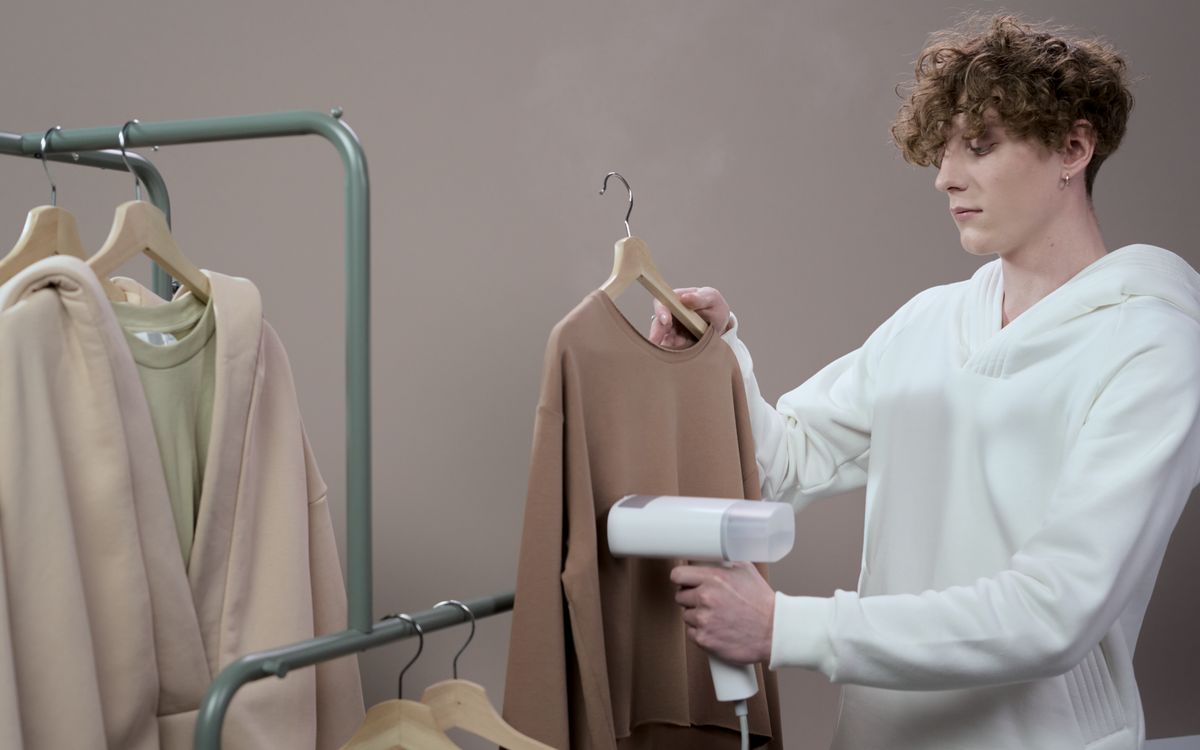 Person steaming a garment with a handheld steamer against a neutral studio background