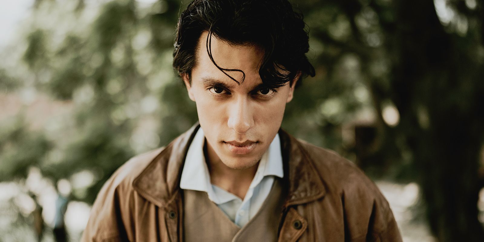 Portrait of a stylish young man wearing a leather jacket posing outdoors in a natural setting
