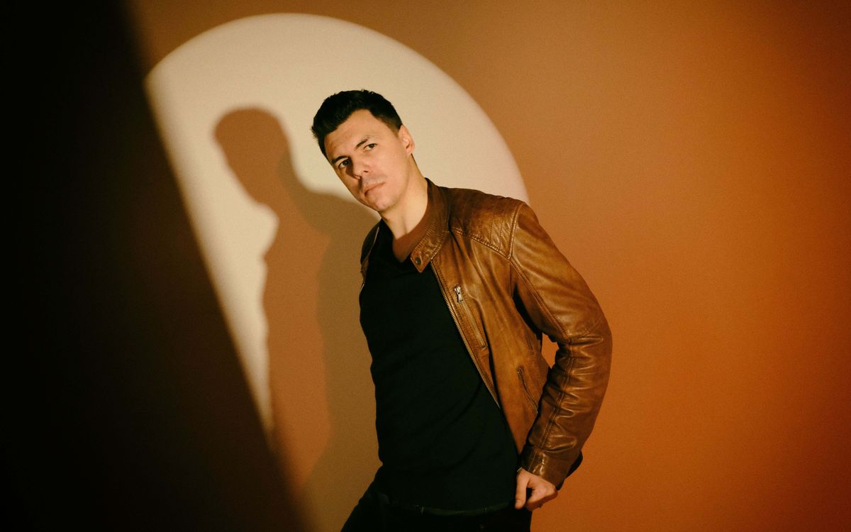 A fashionable man wearing a brown leather jacket posing confidently in a studio setting