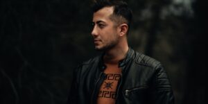 Profile portrait of a man in a black leather jacket against a dark outdoor background