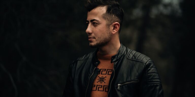 Profile portrait of a man in a black leather jacket against a dark outdoor background