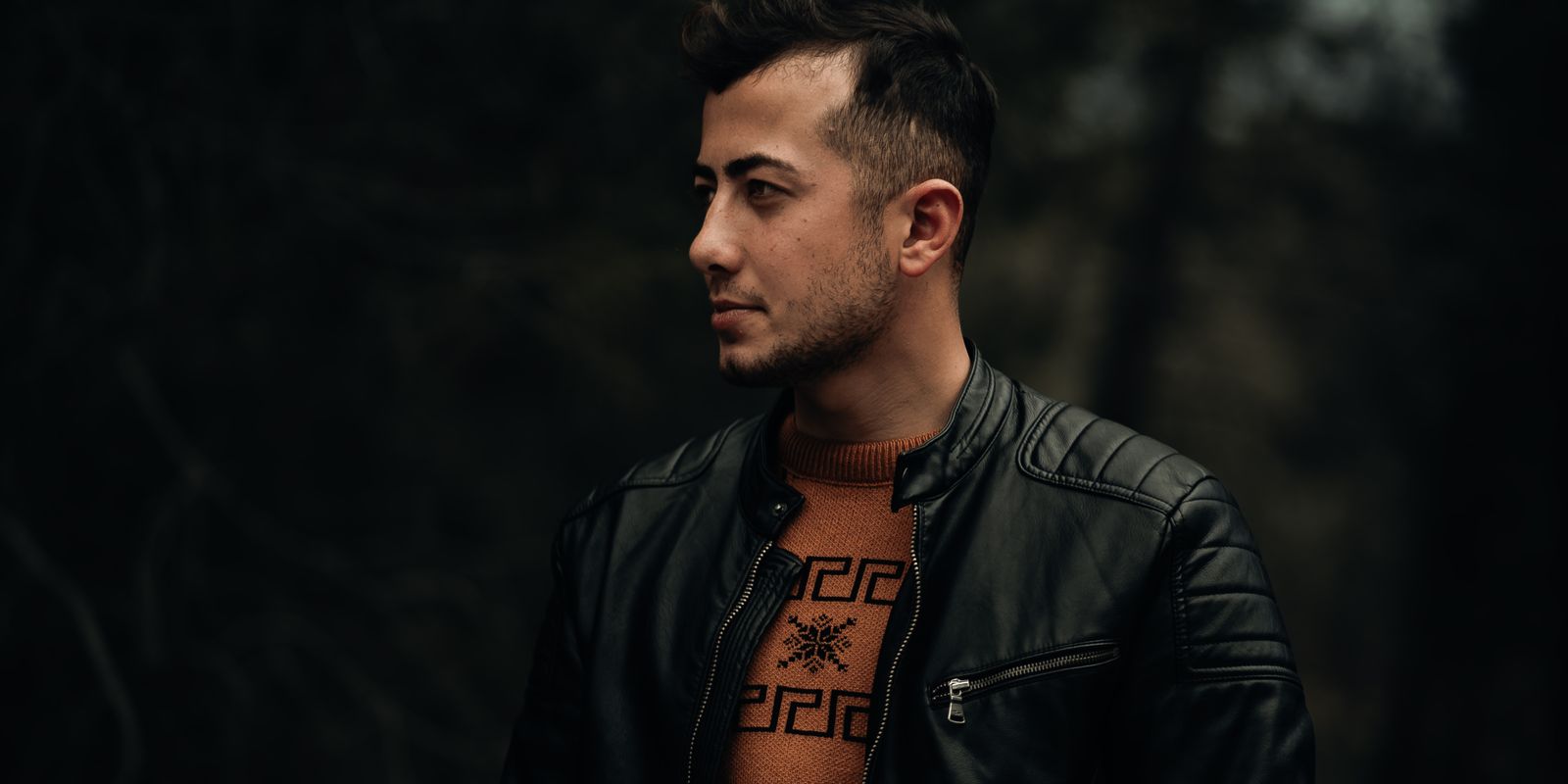 Profile portrait of a man in a black leather jacket against a dark outdoor background