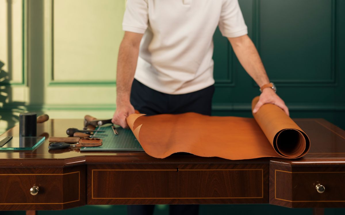 Artisan preparing leather on a workbench with traditional crafting tools in a workshop