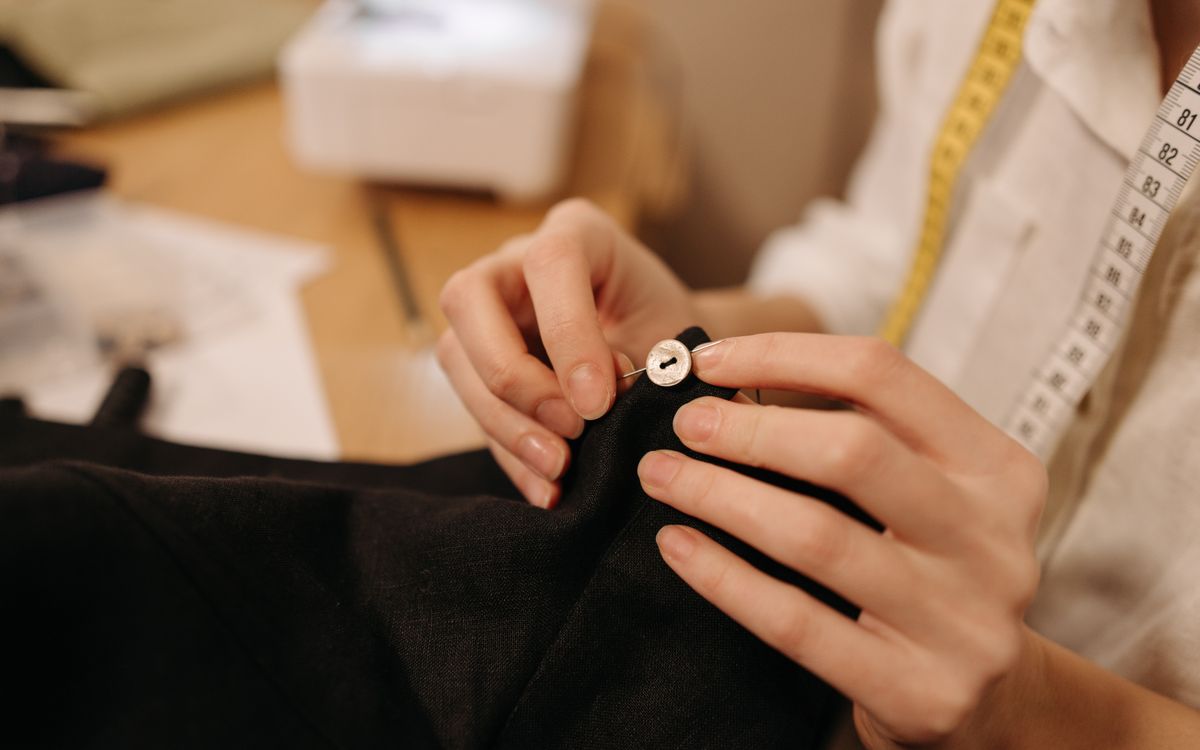 Close-up of a tailor's hands sewing a button with a needle and thread