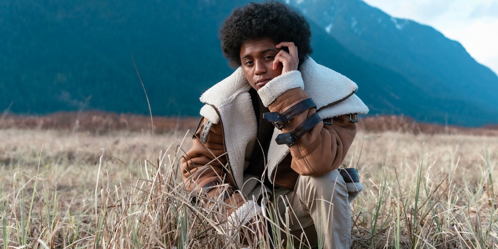 A man wearing a leather jacket with a shearling collar standing in a mountain landscape