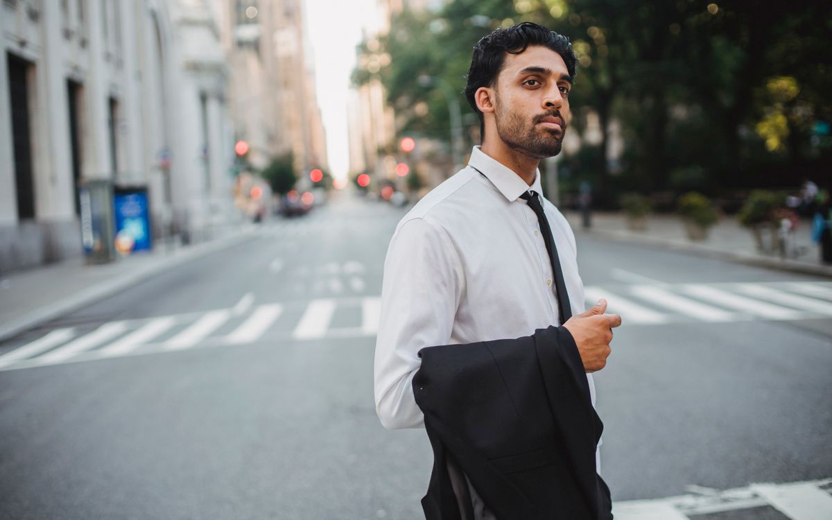 A confident businessman crossing a city street, holding a suit jacket on a bright day