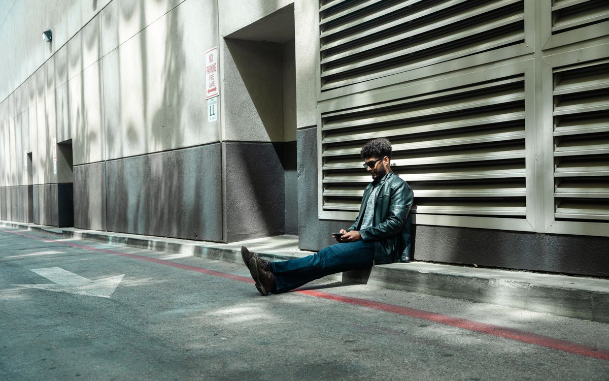 Stylish person in sunglasses and a leather jacket sitting on an urban street