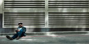 A stylish person in sunglasses and a leather jacket sitting on an urban street