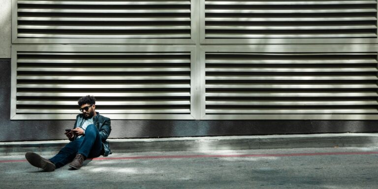 A stylish person in sunglasses and a leather jacket sitting on an urban street