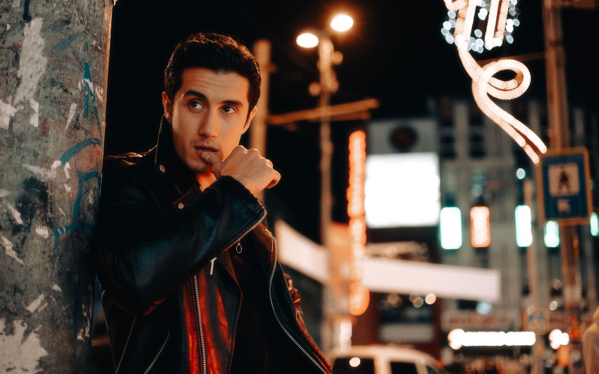 A stylish man posing in a leather jacket on a city street at night
