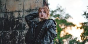 Stylish young woman in a leather jacket posing outdoors against an urban backdrop