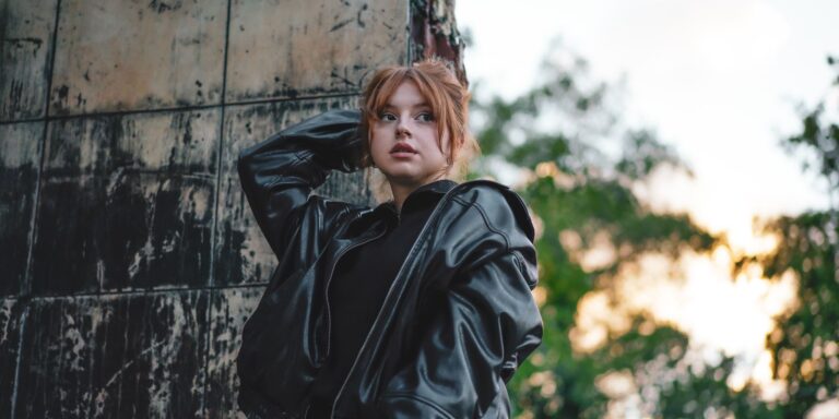 Stylish young woman in a leather jacket posing outdoors against an urban backdrop