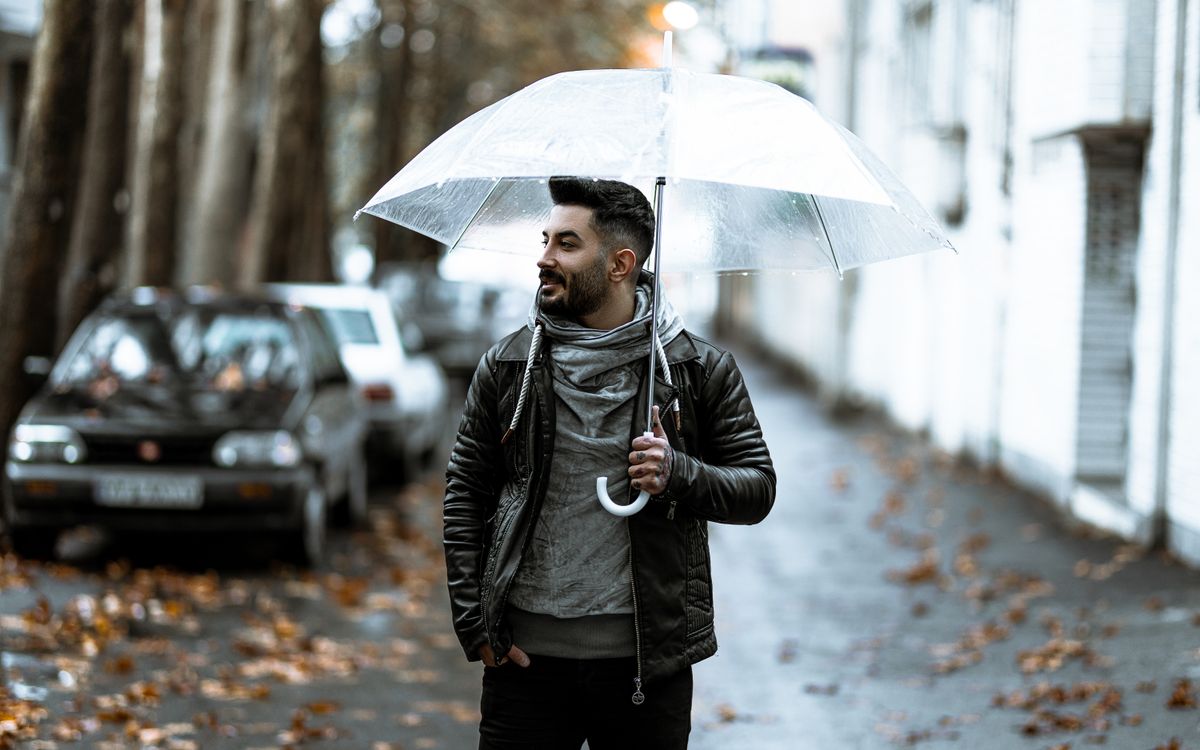A confident man holding a transparent umbrella on a rainy city street