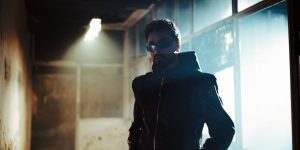 A stylish man in a black leather jacket standing in a dimly lit hallway