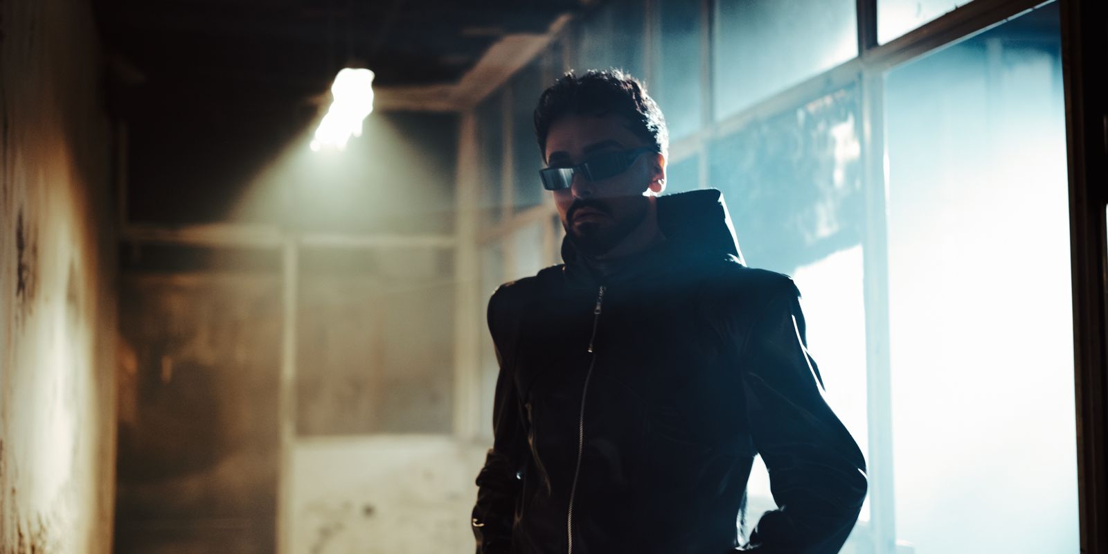 A stylish man in a black leather jacket standing in a dimly lit hallway