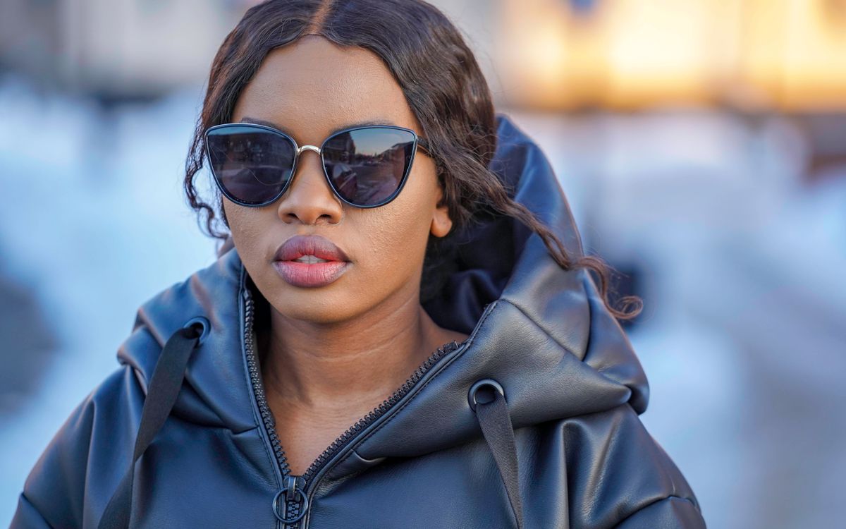 A woman in sunglasses and a black leather jacket against a soft background