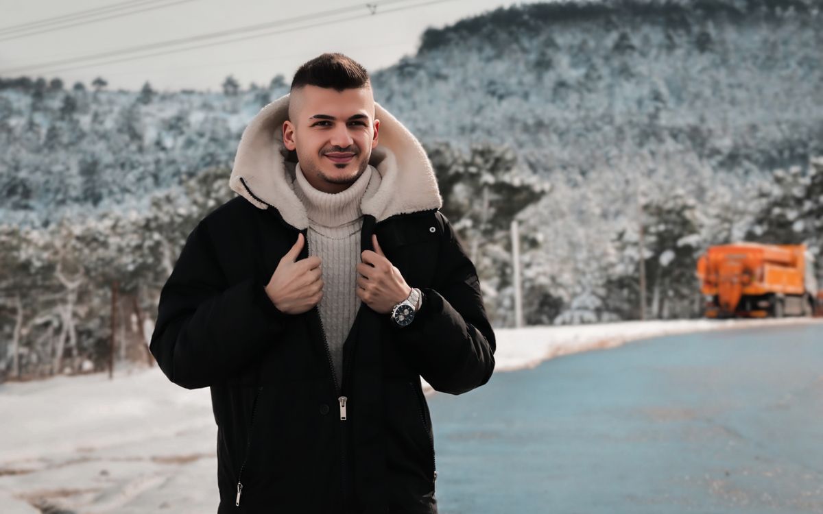 A young man in winter attire standing against a snowy forest background