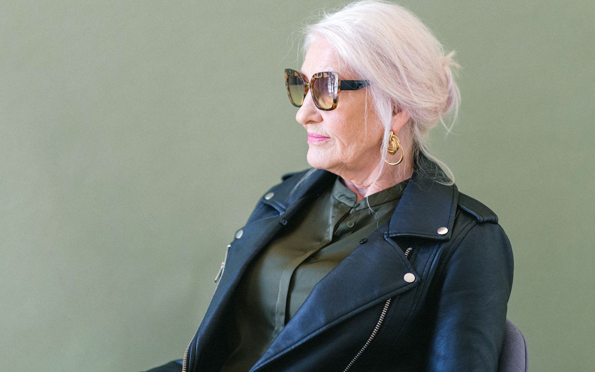 Confident woman in a stylish leather jacket and sunglasses against a green background